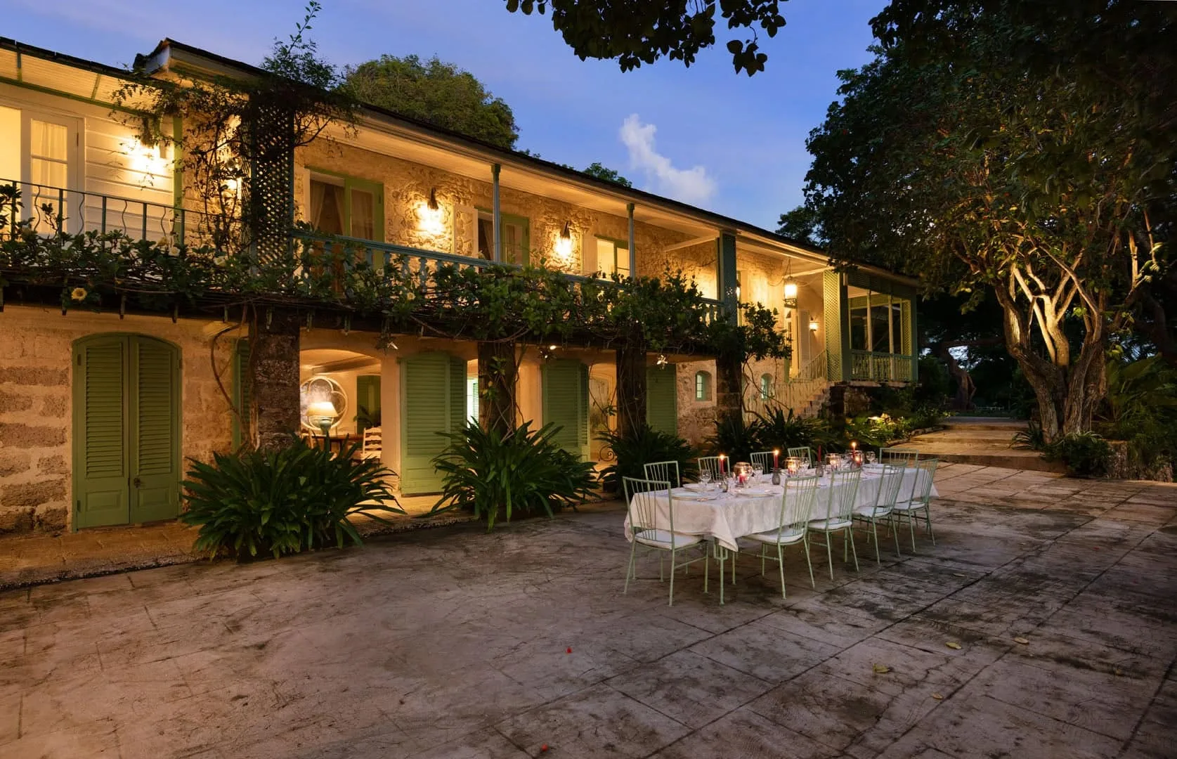 A warmly lit two-story building faces a paved courtyard with an outdoor dining table.