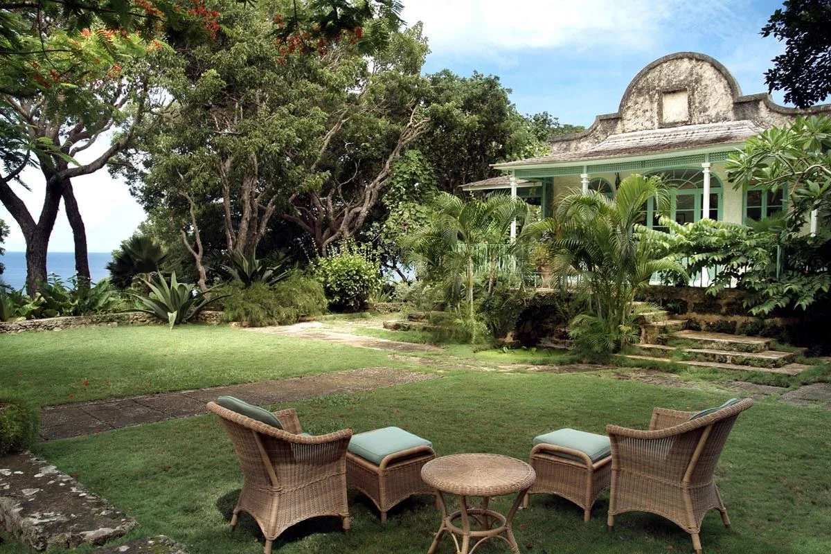 A garden lawn with wicker seating faces a leafy veranda.
