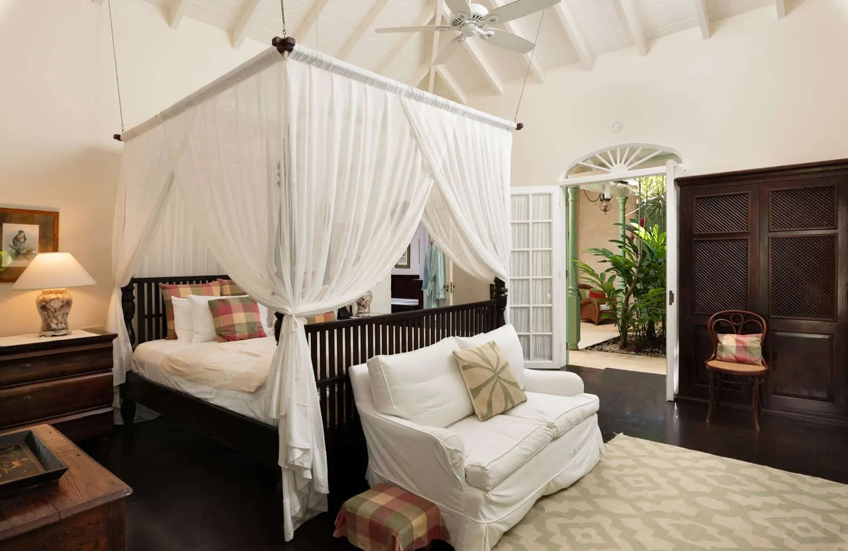 A bedroom with a curtained canopy bed and a white seating area.