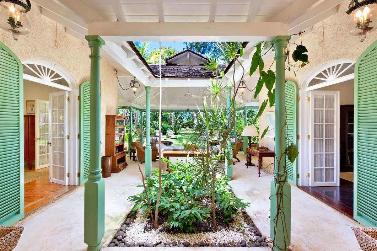 A bright tropical courtyard with plants, green columns, and open doorways.