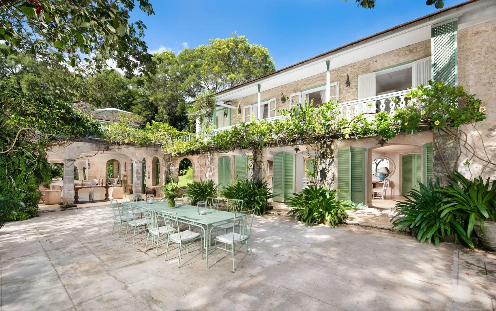 A sunny courtyard with outdoor seating, leafy plants, and a two-story building.