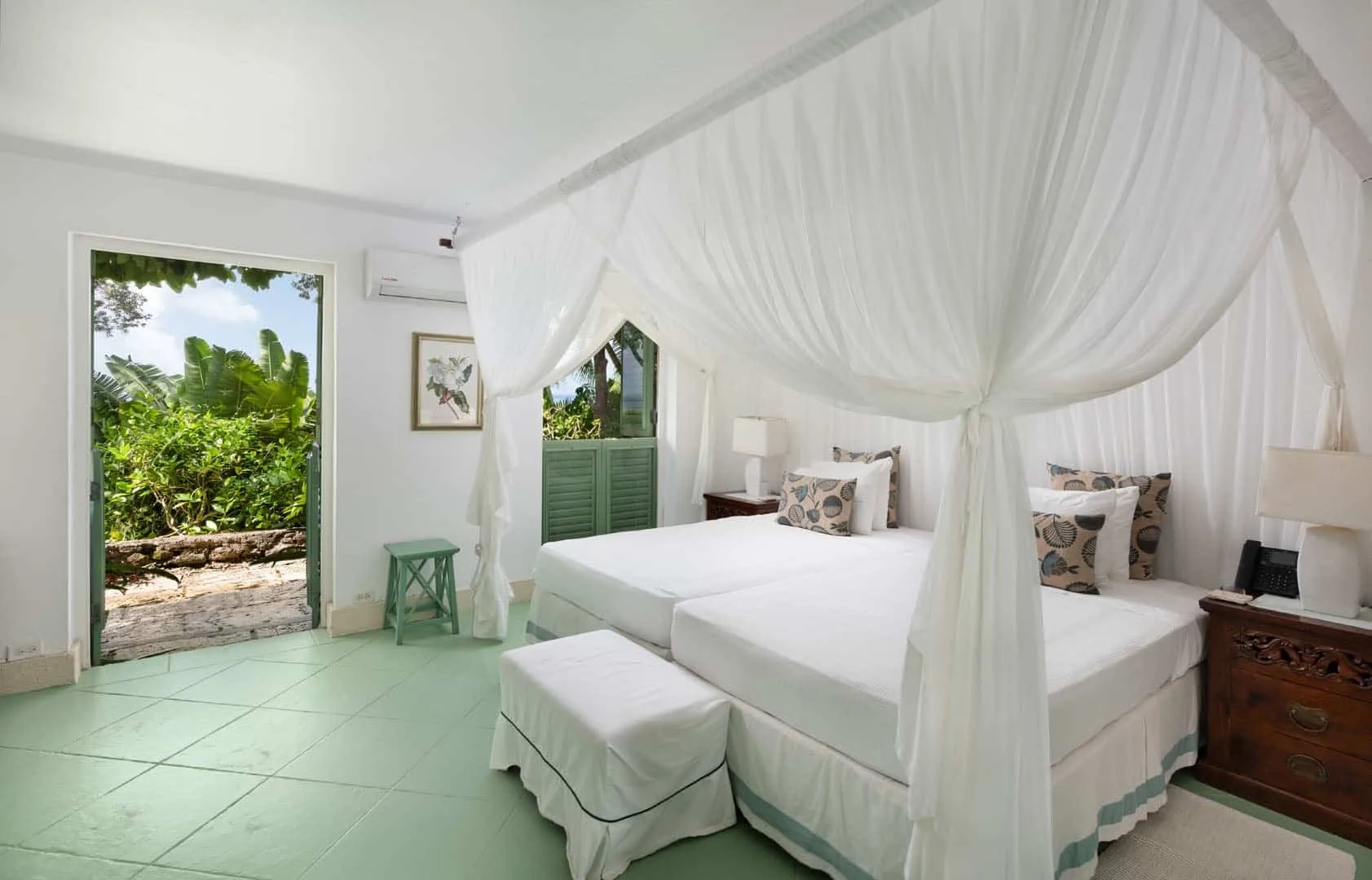 A bright bedroom with a white canopy bed and garden views through an open doorway.