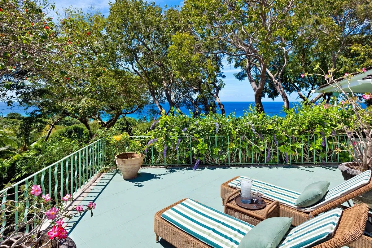 A seaside patio with striped loungers, leafy trees, and ocean views.