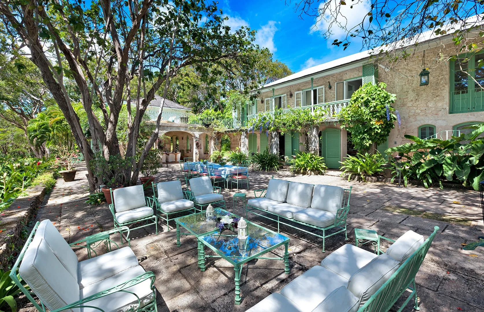An outdoor patio with seating and a glass-topped table beside a leafy building.