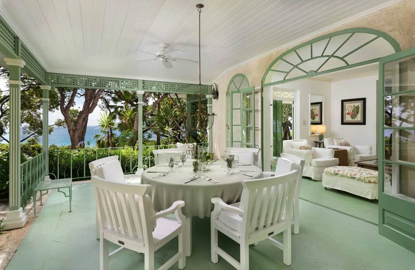 A covered dining area opens onto a veranda overlooking trees and the water.