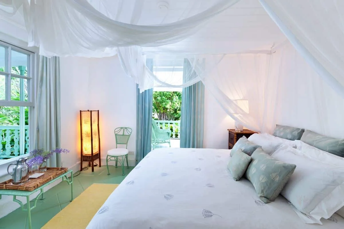 A bright bedroom with a large bed and sheer white canopy drapes.