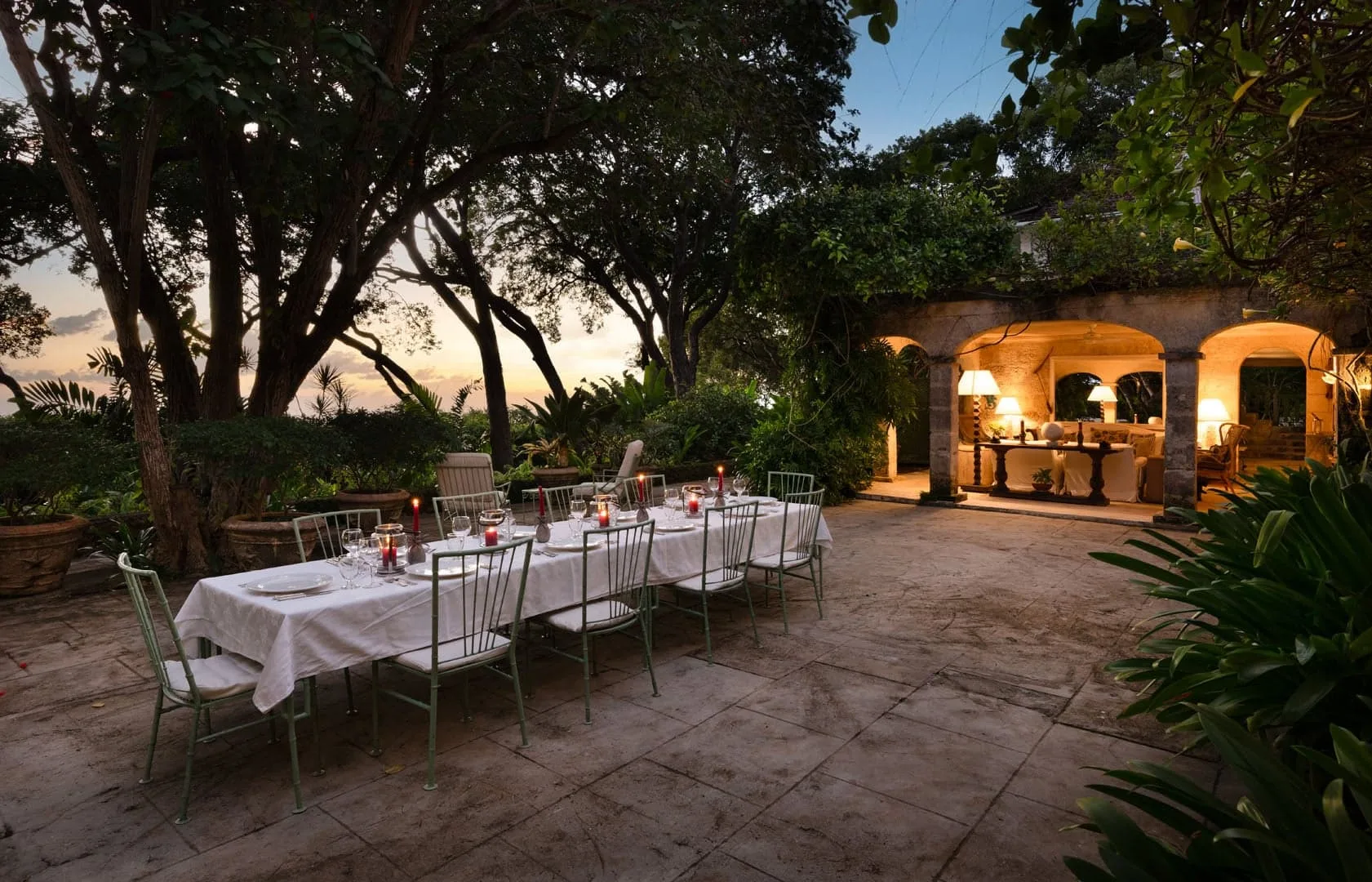 An outdoor dining area with a set table beneath trees and a warmly lit bar.