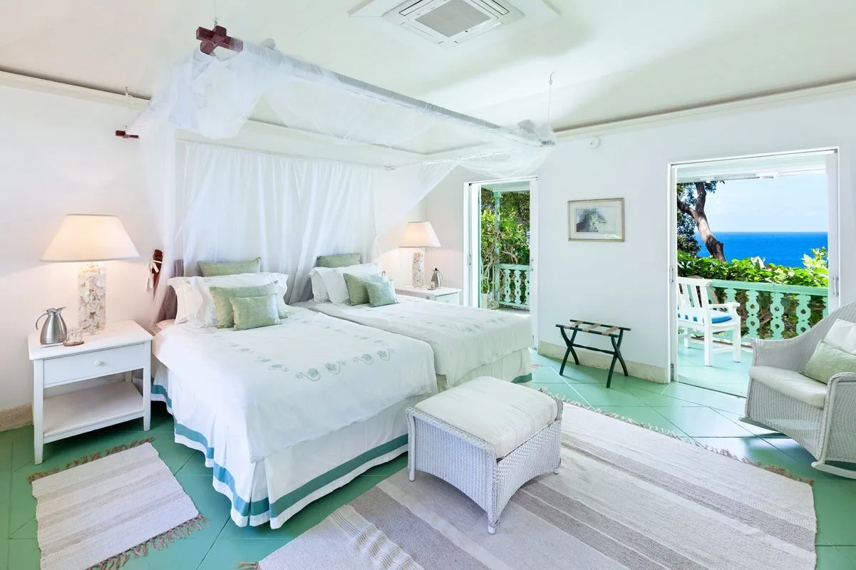 A bright bedroom with white bedding and open doors overlooking the sea.