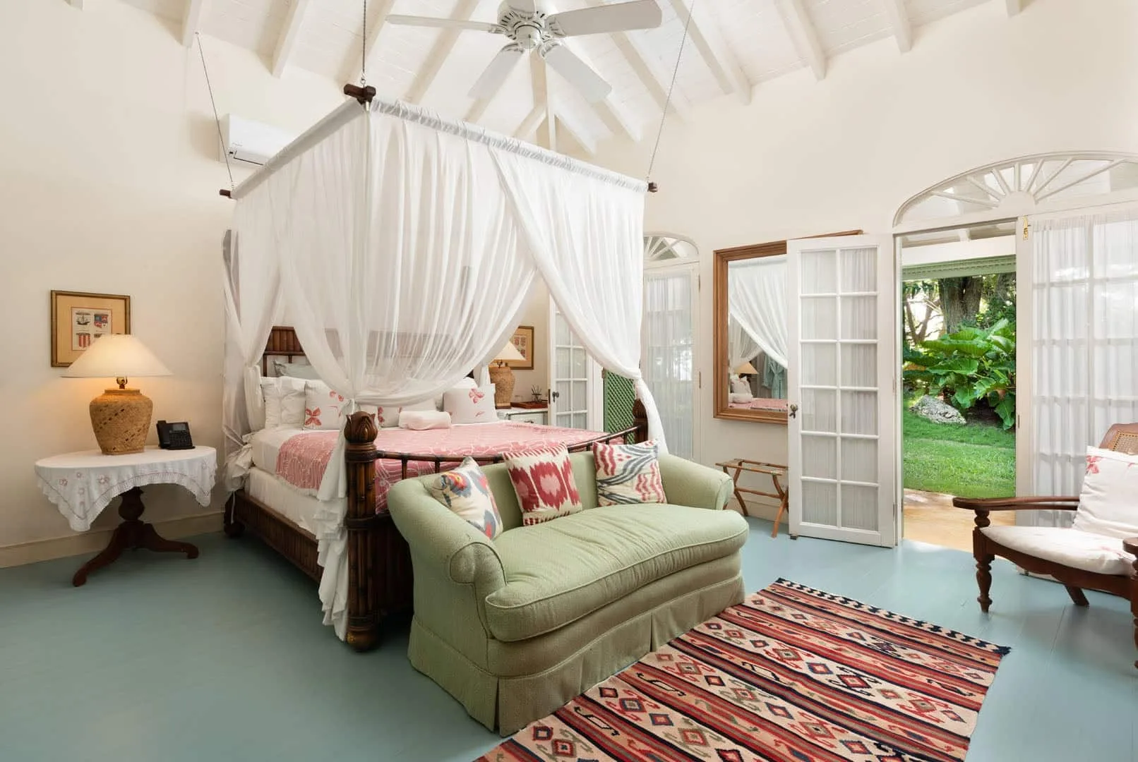 A bright bedroom with a draped canopy bed and a pale green loveseat.