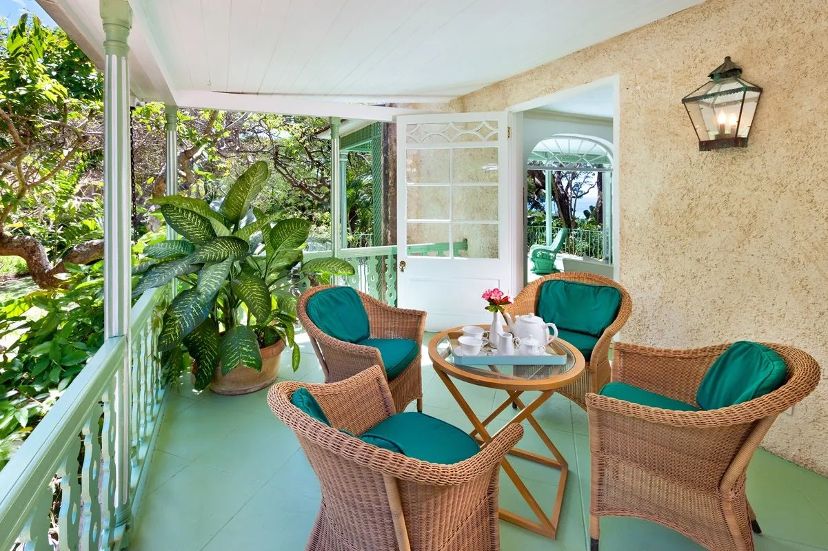 A covered patio with wicker seating and lush plants.