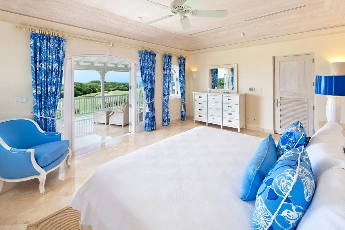 Un dormitorio luminoso con una cama grande, asientos azules y puertas que dan a un balcón.