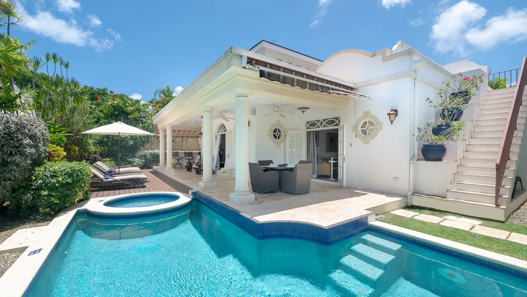 A swimming pool beside a white house with a covered patio and outdoor seating.