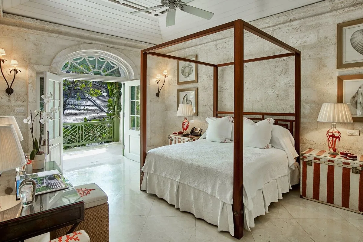 Dormitorio con una cama con dosel junto a puertas abiertas que dan a un balcón frondoso.