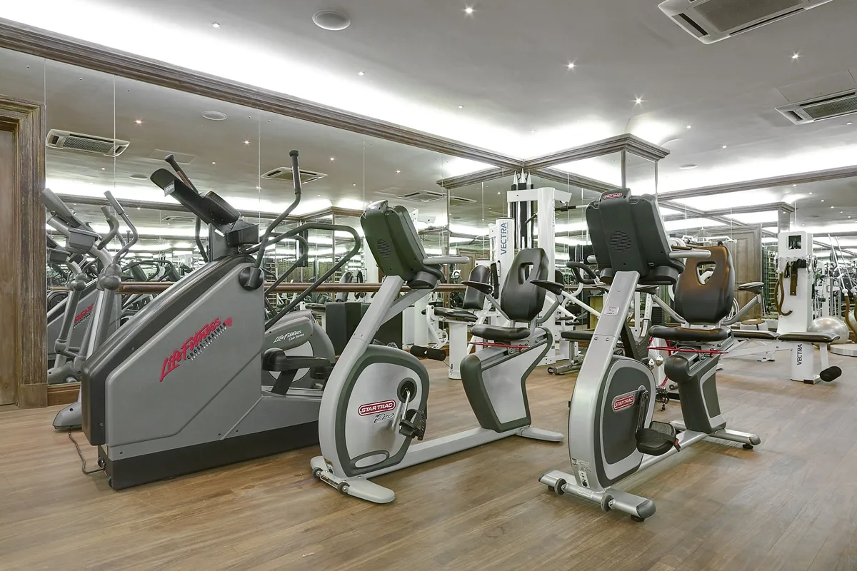Un gimnasio con máquinas de ejercicio en una zona de entrenamiento con espejos.