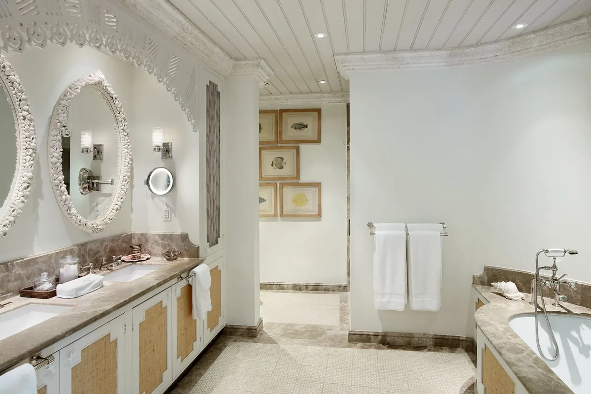 Un baño luminoso con un tocador largo, espejos decorativos y toallas en la pared.