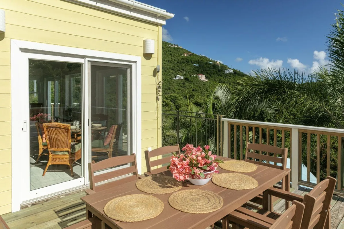 Una mesa de comedor de madera está en una terraza junto a puertas corredizas de vidrio.
