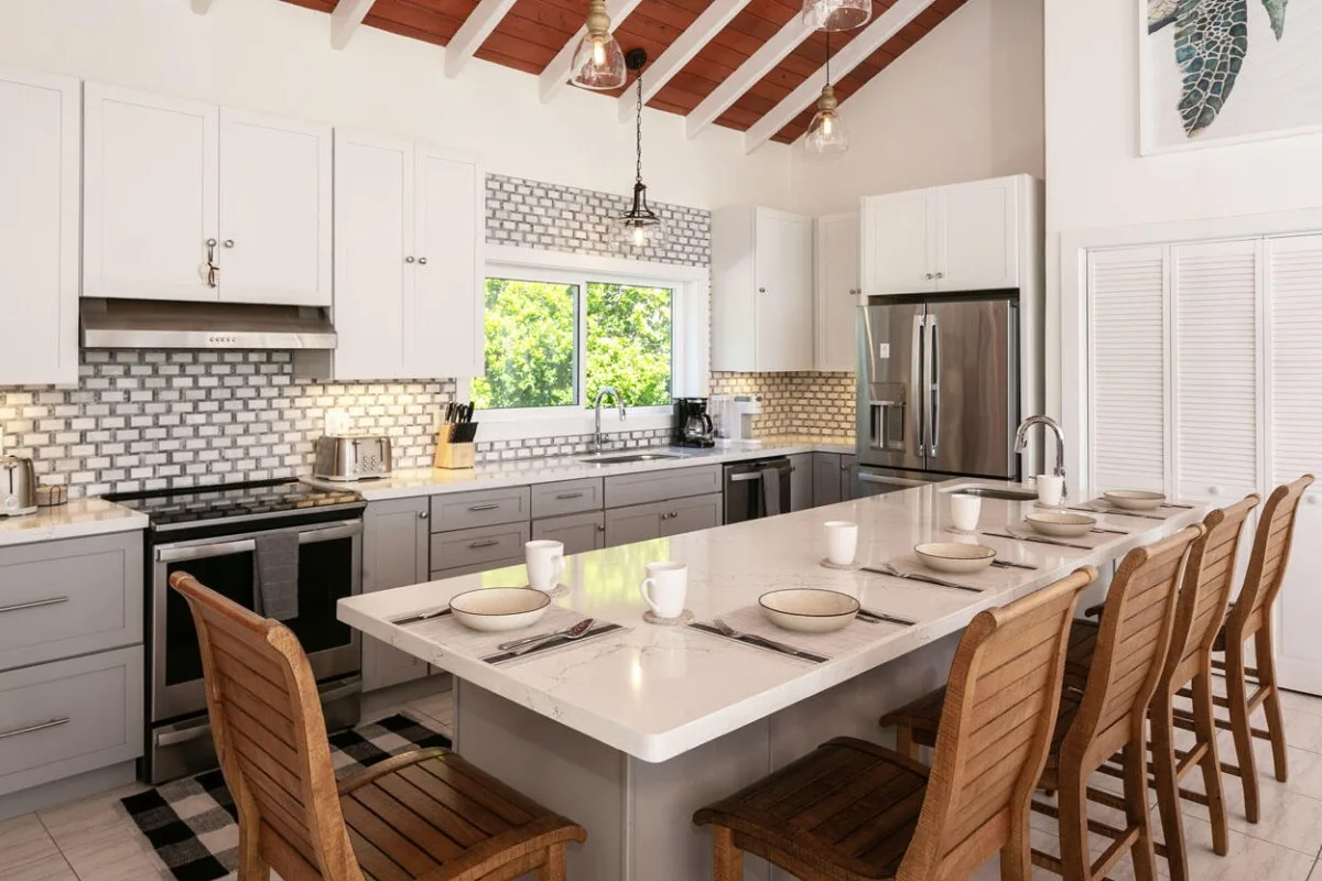 Una cocina luminosa con gabinetes blancos, una isla central y asientos de madera.