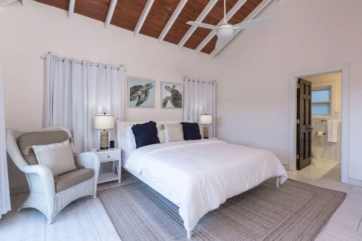 Un dormitorio luminoso con una cama grande, mesitas de noche y un sillón.