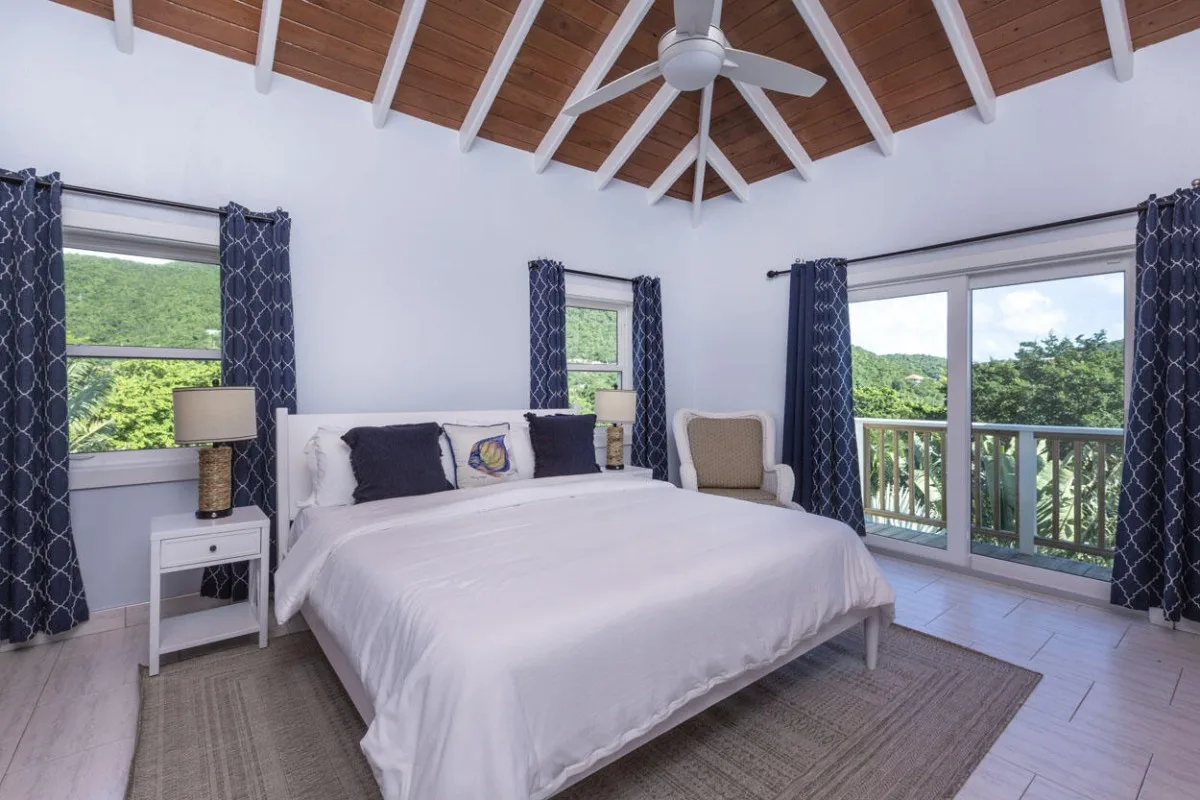 Un dormitorio luminoso con una cama bajo un techo abovedado de madera y grandes ventanas.