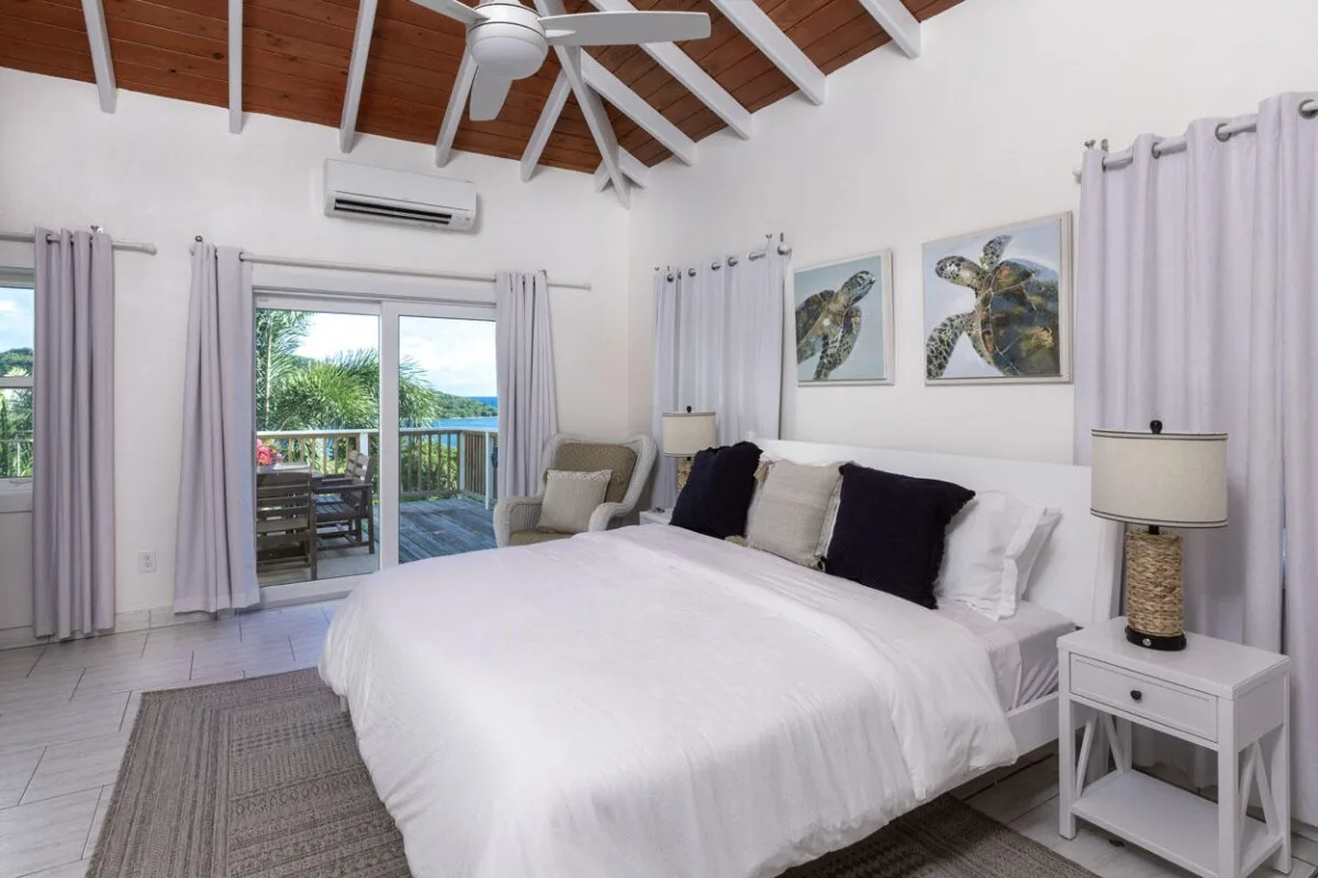 Un dormitorio luminoso con una cama grande, cortinas claras y un techo abovedado de madera.