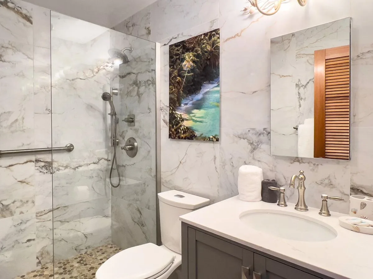 Un baño de mármol con ducha de vidrio, inodoro y tocador.