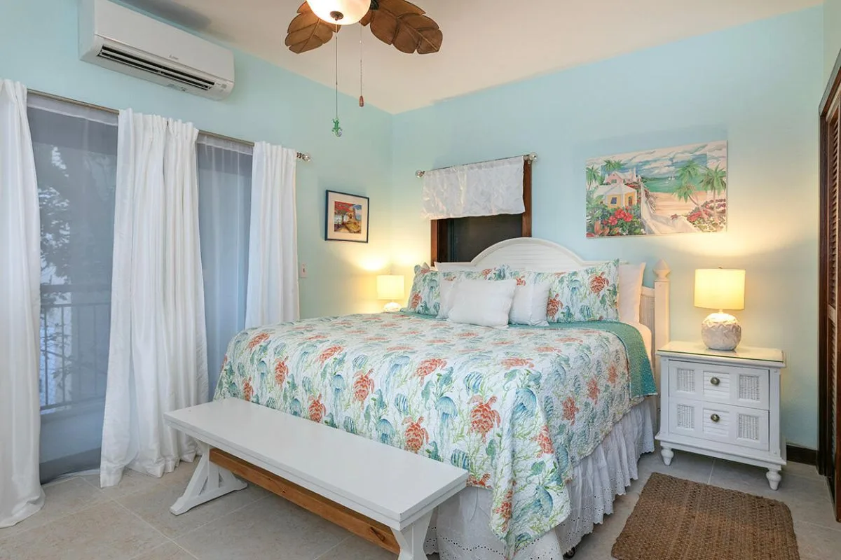Un dormitorio con una colcha floral, cortinas blancas y lámparas de mesilla a juego.
