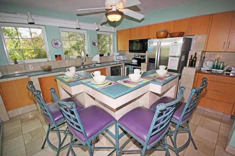 A spacious kitchen has a central counter set with dishes and surrounded by seating.