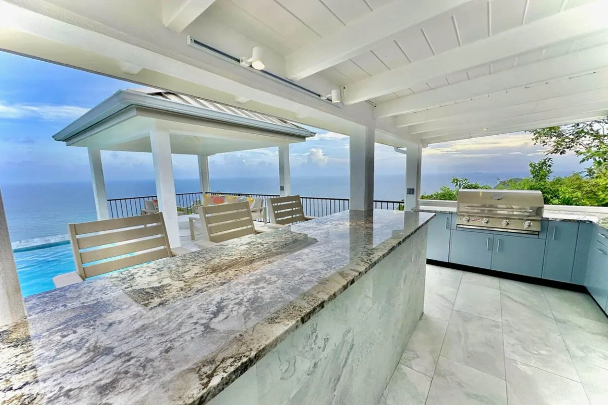 A covered outdoor kitchen and bar counter overlook the ocean.
