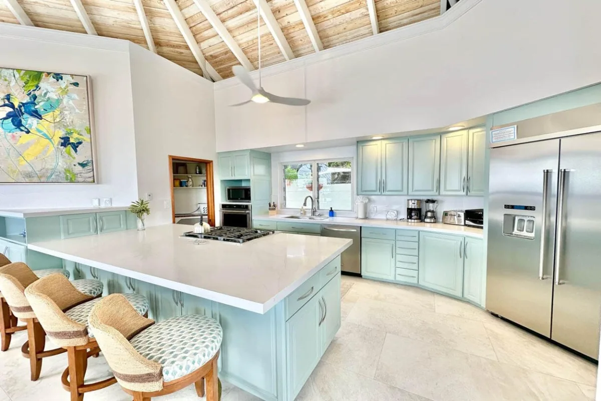 A bright kitchen with pale blue cabinets, a large island, and a vaulted ceiling.