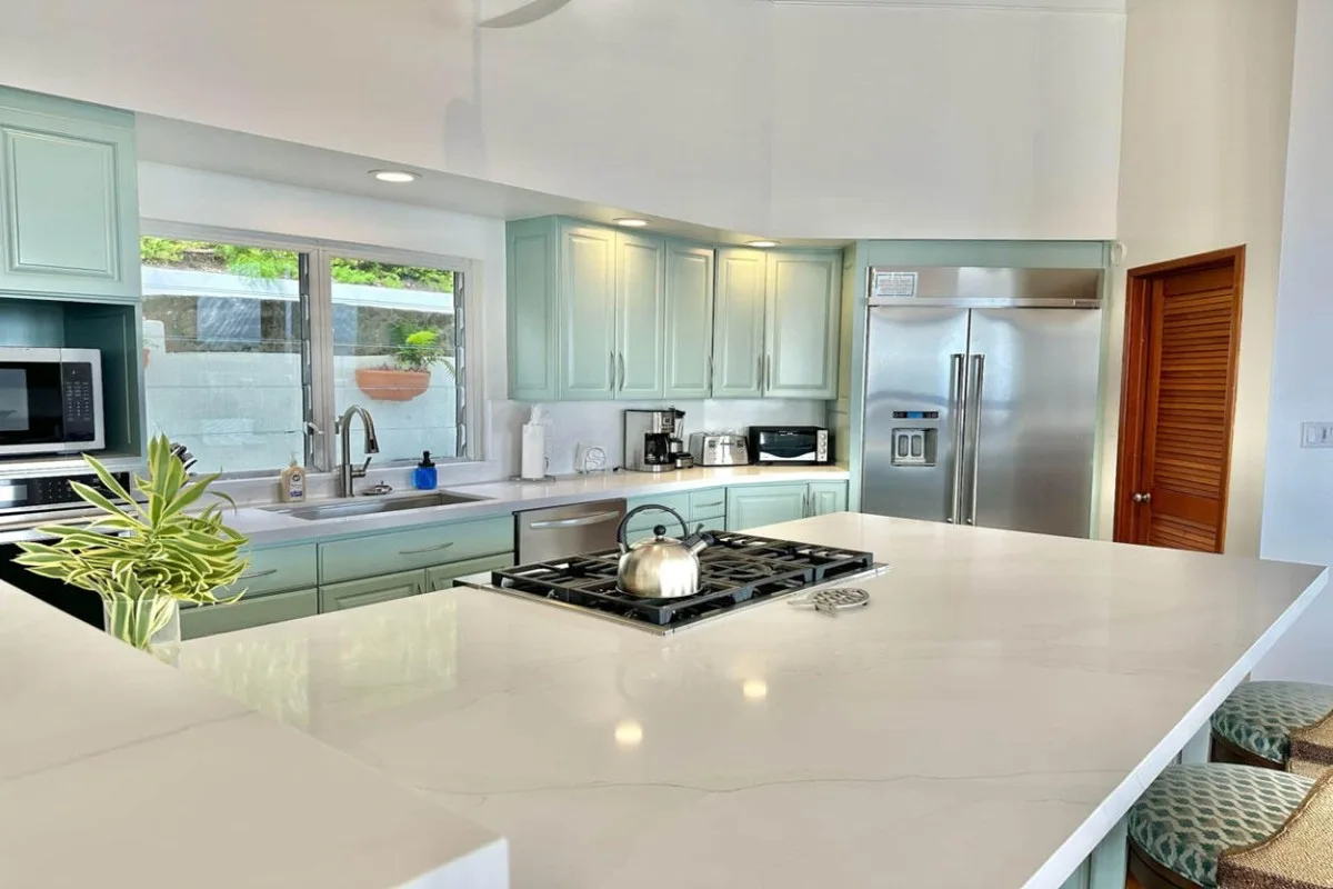 A bright kitchen with pale cabinets, a large island, and stainless steel appliances.