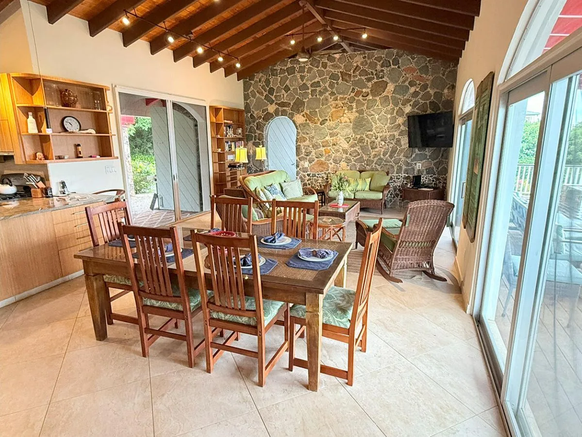 A dining and living area with a wooden table and seating beside a stone wall.