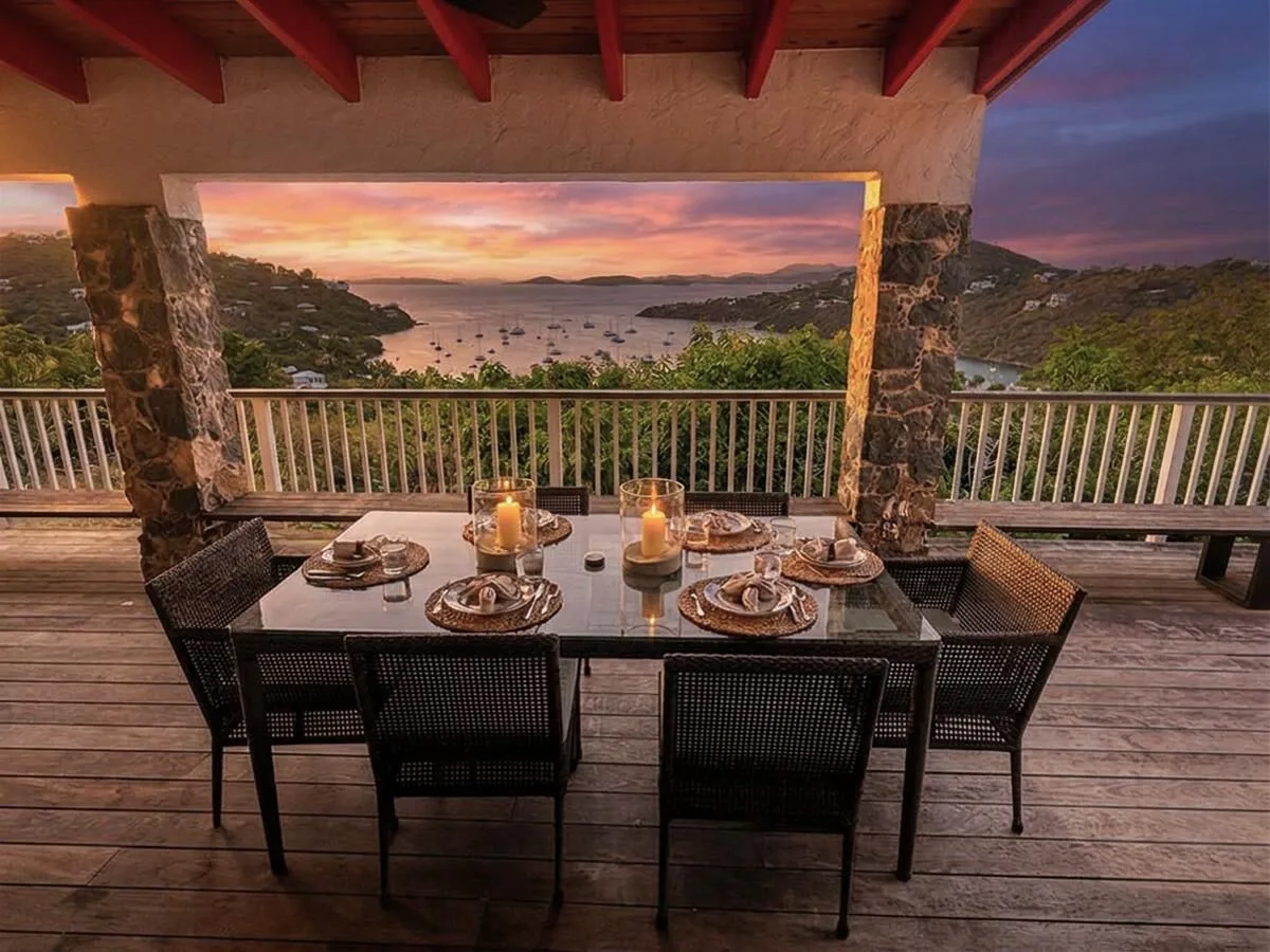 A covered outdoor dining area overlooks a bay at sunset.