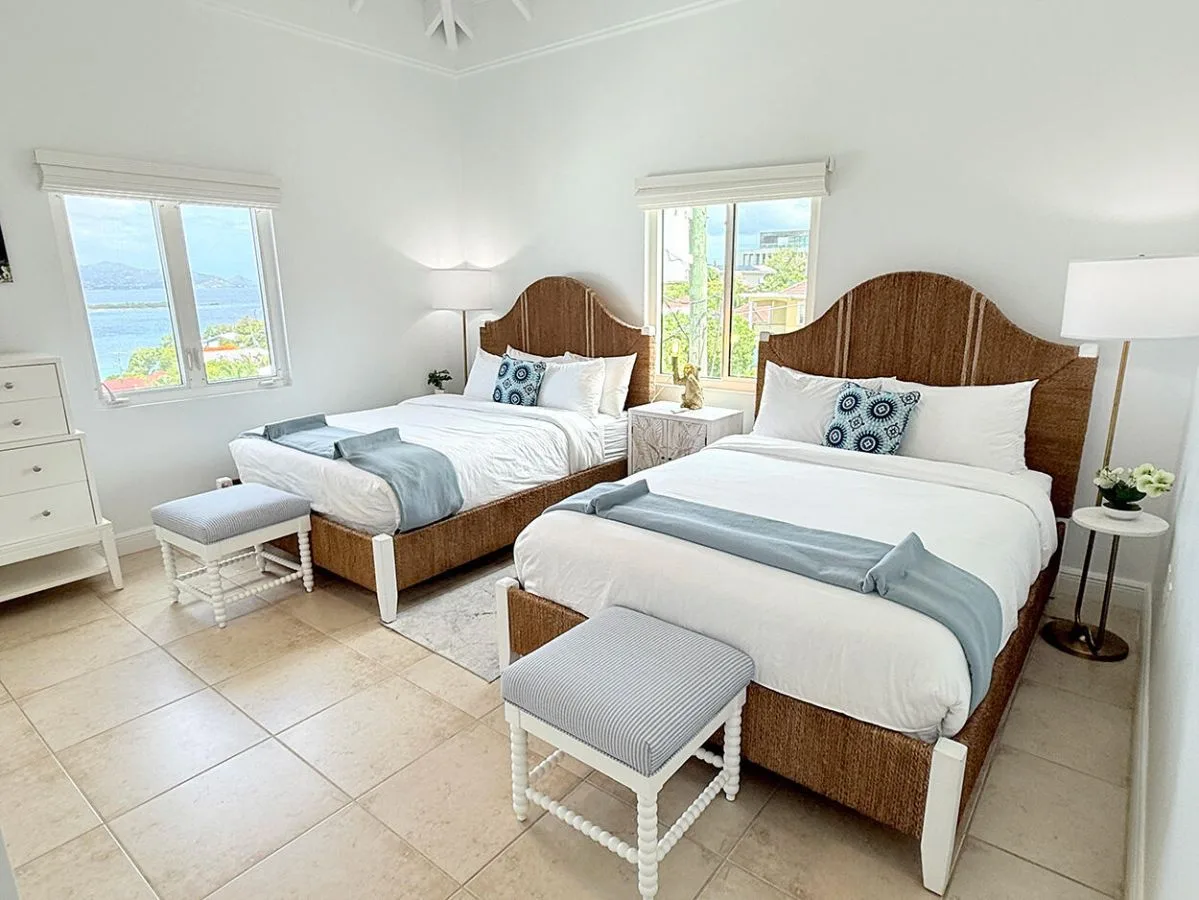 Un dormitorio luminoso con dos camas y grandes ventanas con vistas al agua.