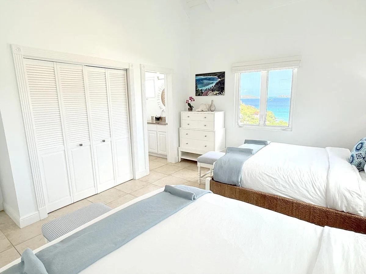 Un dormitorio luminoso con dos camas y una ventana con vistas al mar.
