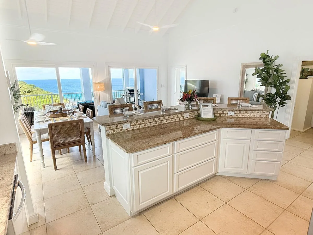Una cocina luminosa con una amplia isla y comedor junto a ventanas con vistas al agua.