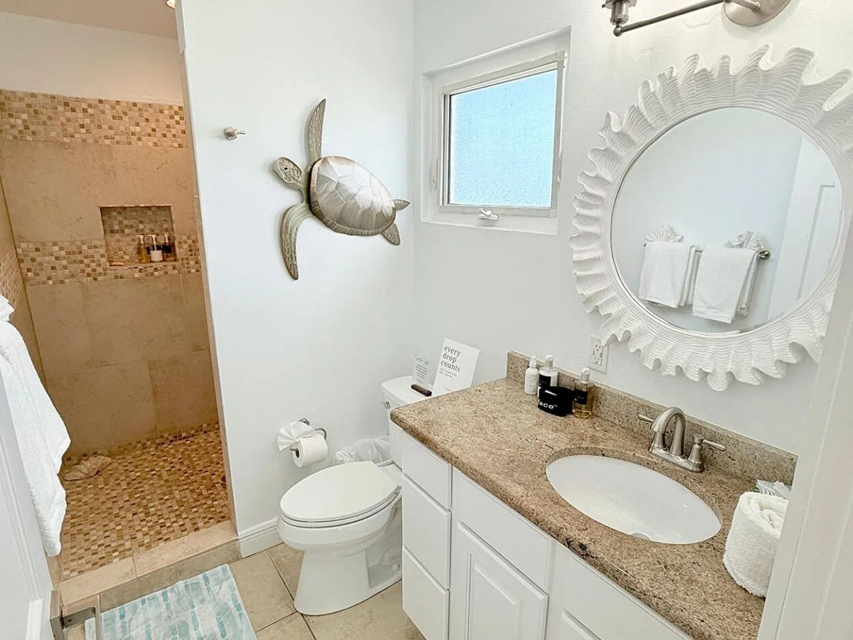Un baño con ducha de azulejos, inodoro y lavabo junto a un espejo redondo.