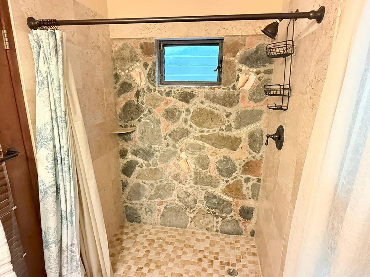 Una ducha con azulejos, una pared de piedra y una ventana pequeña.