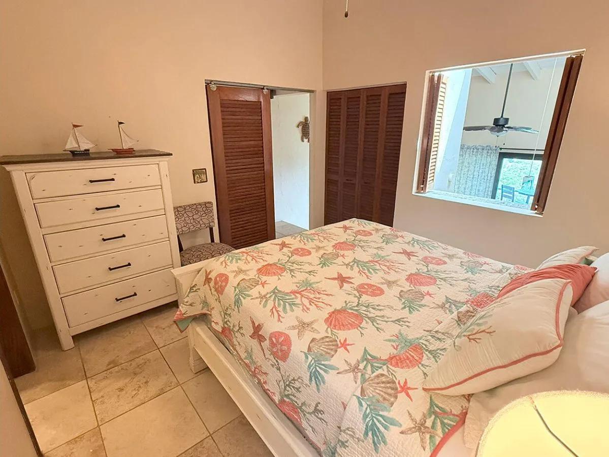 Un dormitorio con una colcha floral, una cómoda y una ventana.