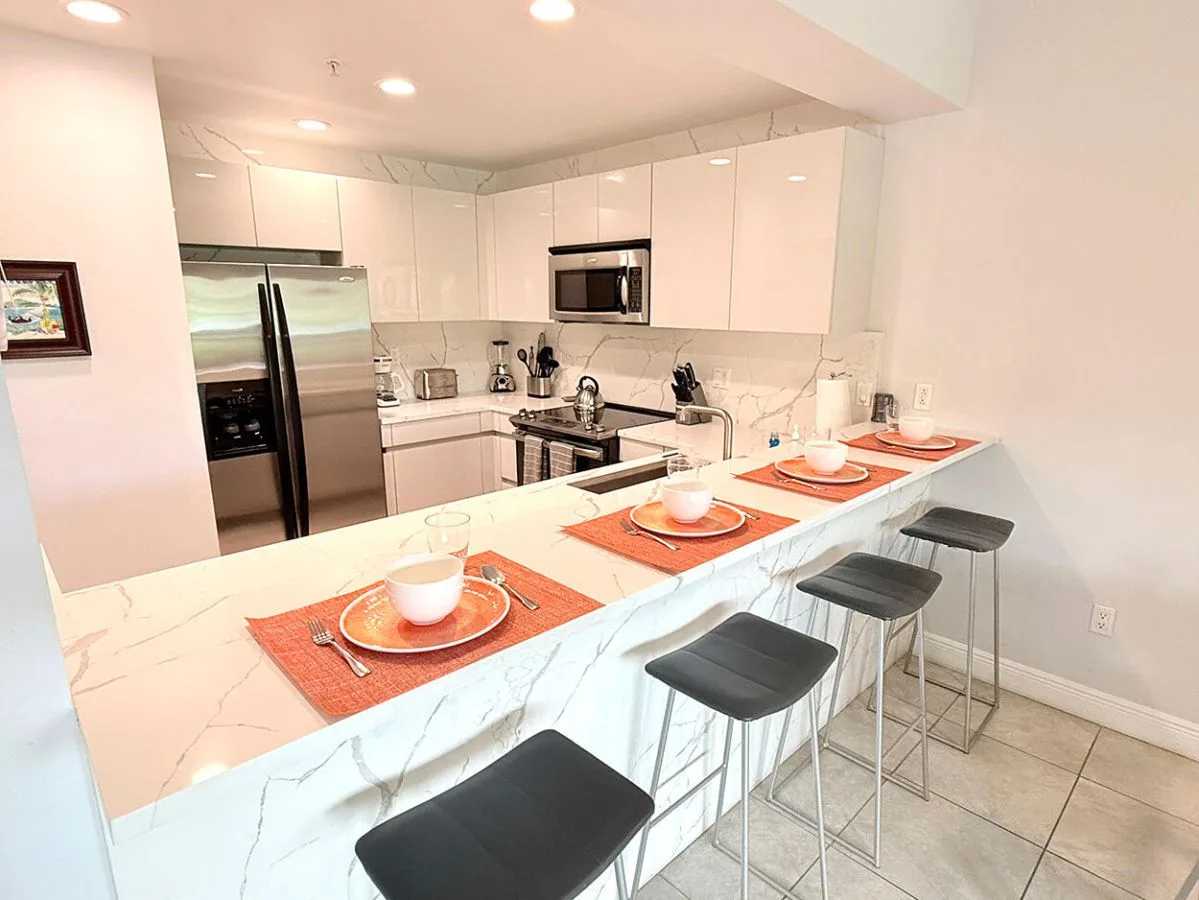 Una cocina luminosa con gabinetes blancos y una isla larga con taburetes.