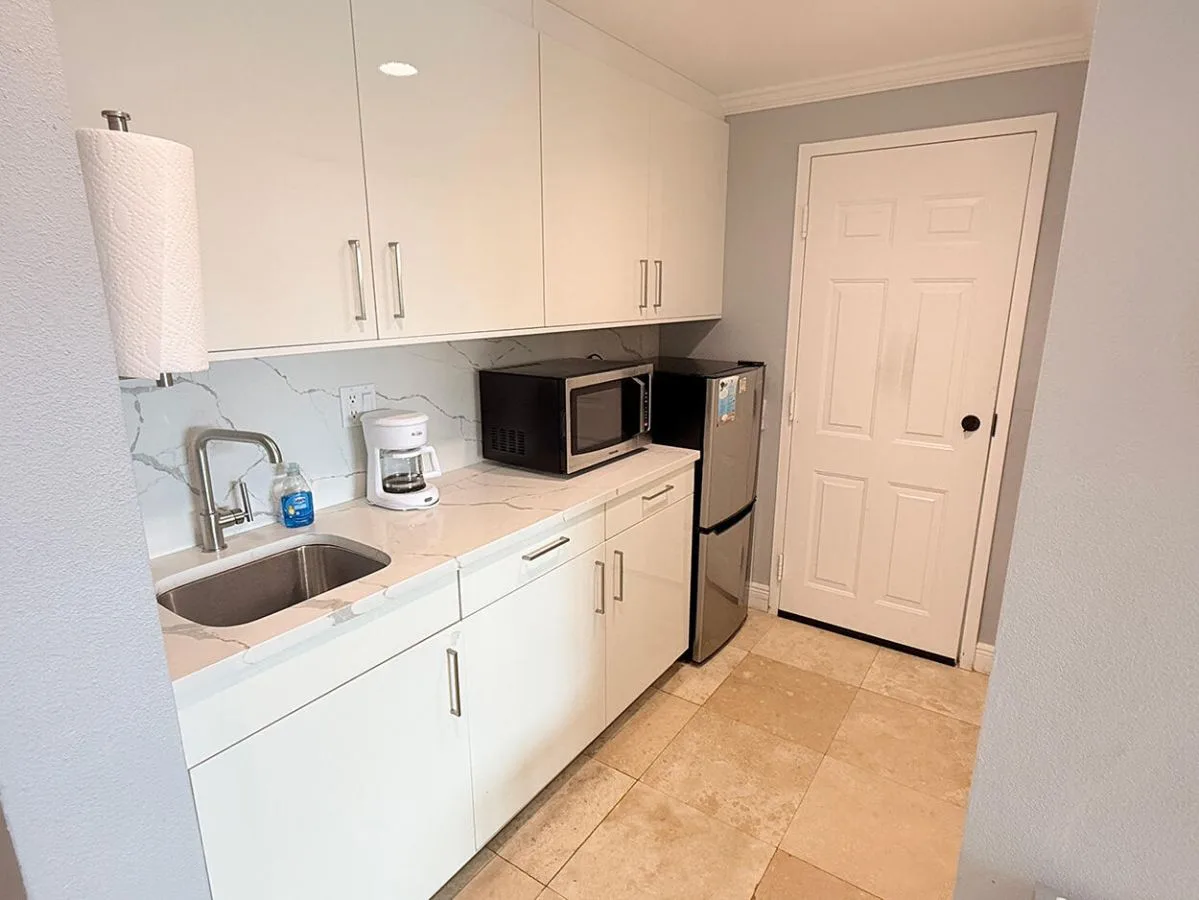 Una cocina compacta con gabinetes blancos, una encimera y un refrigerador.