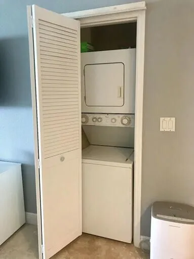 Una zona de lavandería con lavadora y secadora apiladas detrás de una puerta abierta con celosías.