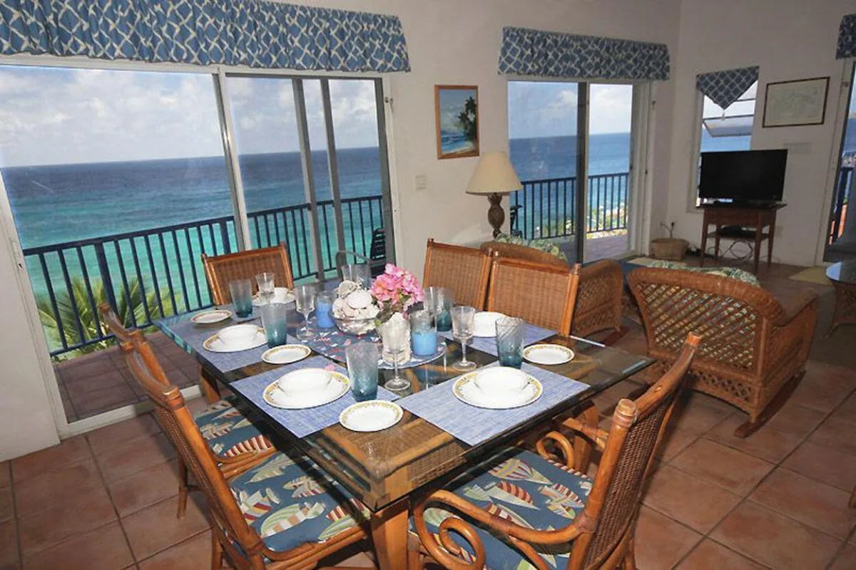 Comedor con una mesa puesta junto a grandes ventanales con vista al océano.
