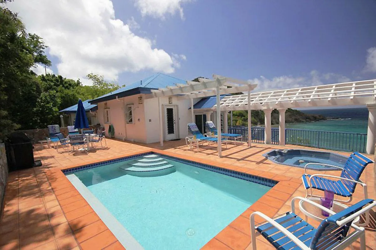 Una terraza con piscina junto a un edificio pequeño, con asientos y una pérgola frente al agua.