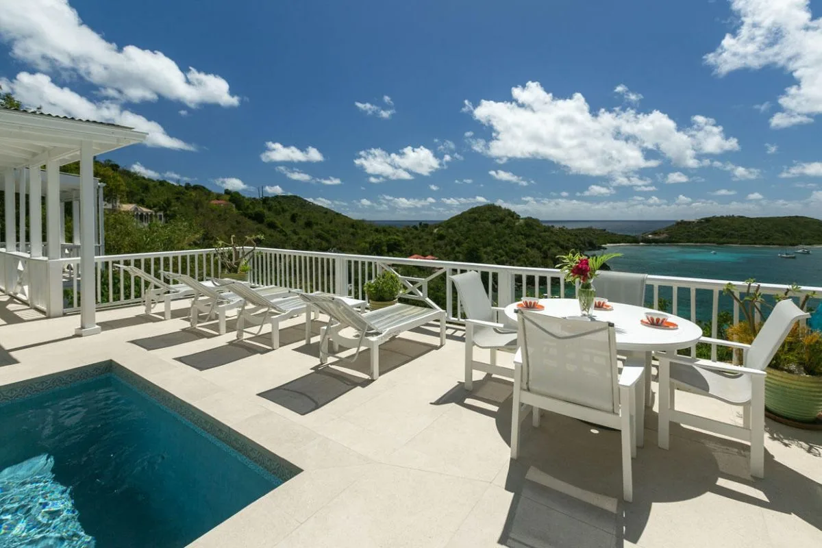 Una terraza soleada junto a la piscina tiene asientos blancos y vistas al agua.