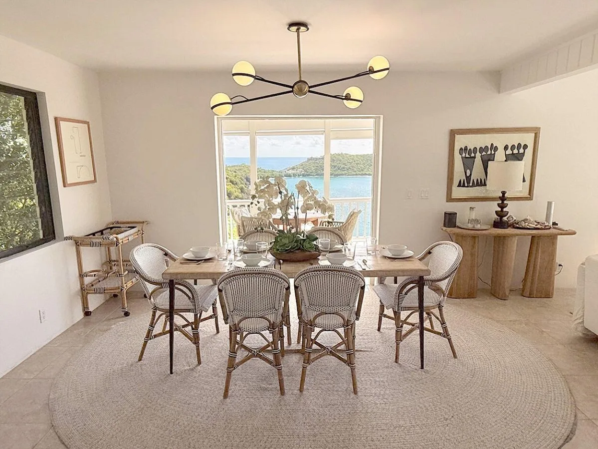 Un comedor luminoso con una mesa y asientos de tejido junto a una ventana grande.