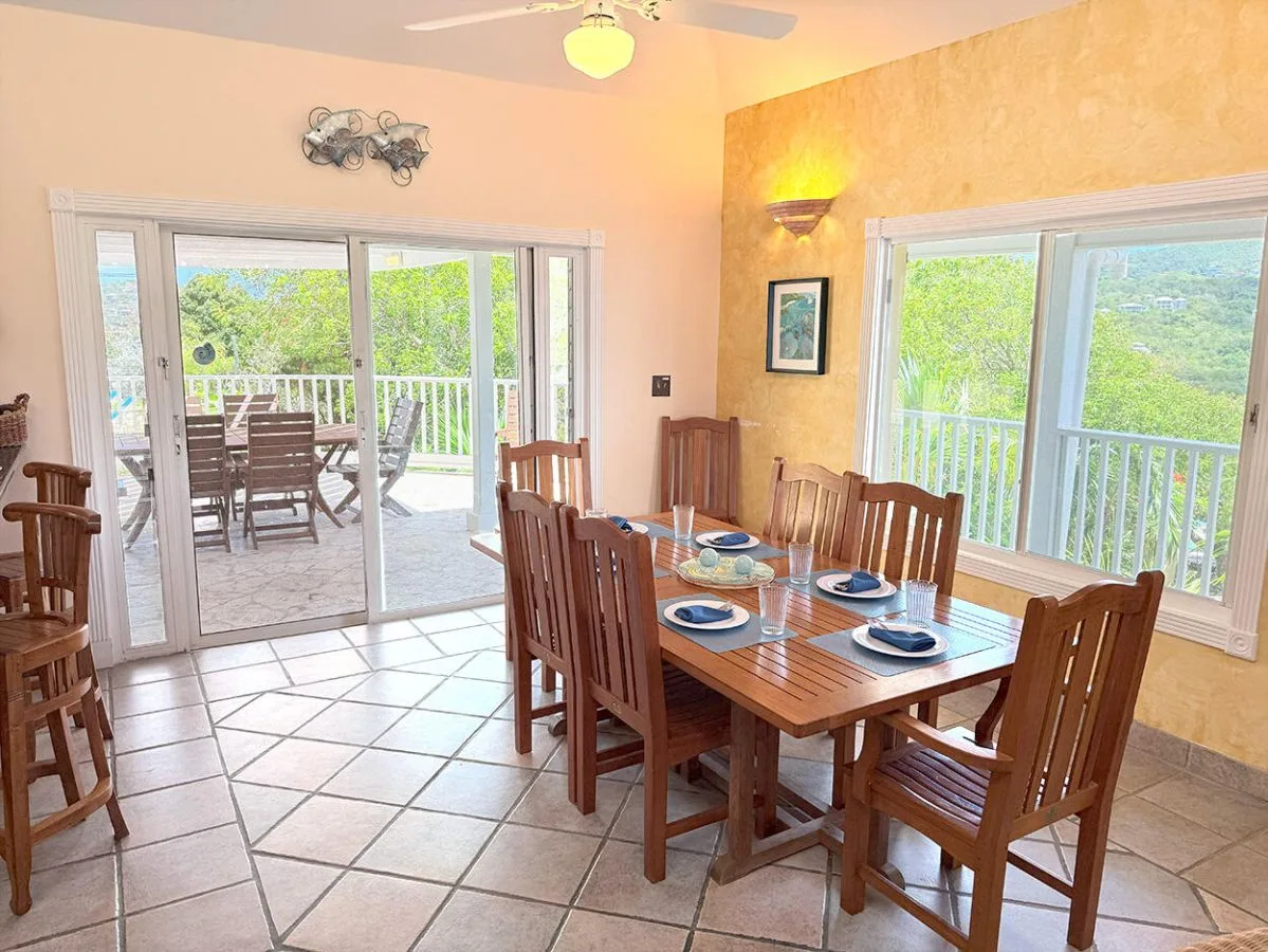 A dining area with a wooden table and large windows overlooking greenery.