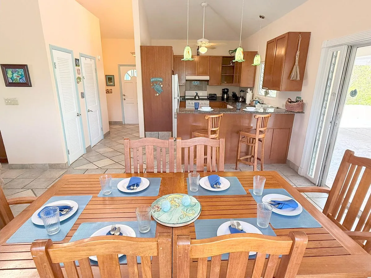 A dining area with a set table opens onto a kitchen with a counter.
