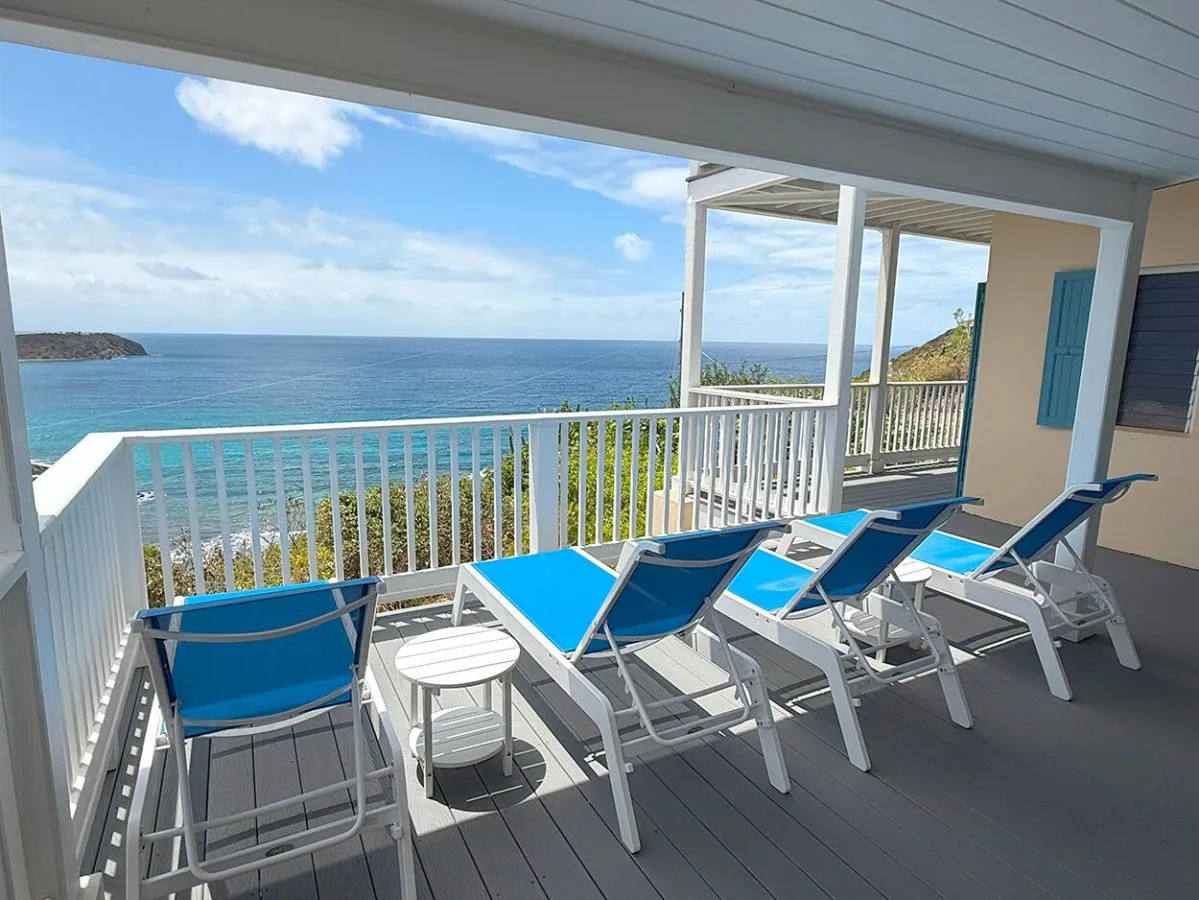 A covered seaside deck with blue lounge seating overlooking the ocean.
