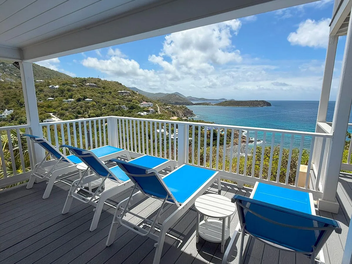 A covered deck with blue loungers overlooks a coastal bay.