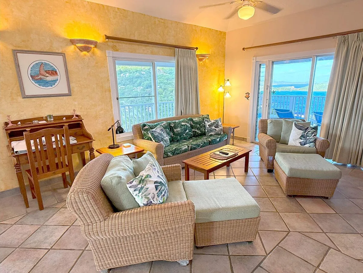 A living room with wicker seating, a desk, and windows overlooking the water.